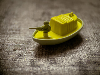Yellow toy boat on a textured surface suitable for childrens book illustration, toy packaging, beachthemed graphics, summer design projects.