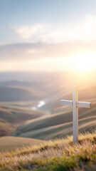 Wooden cross on grassy hill with sunrise over misty mountain valley, peaceful spiritual landscape with warm light