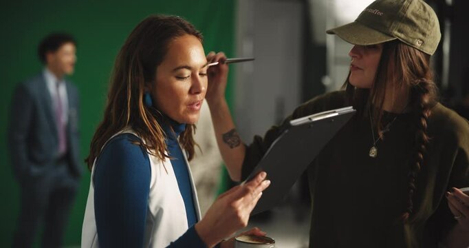 Filming, clipboard and makeup with actress on set for shooting, foundation application and broadcast. Production setup, backstage prep and reading scrip with woman in studio for process and media