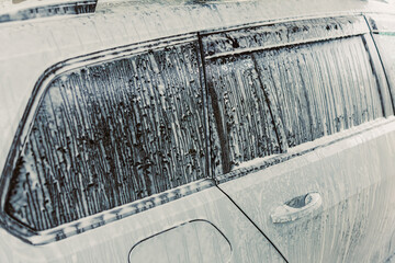 A rainy day scene showcasing a car window adorned with glistening water drops and remnants of soap...