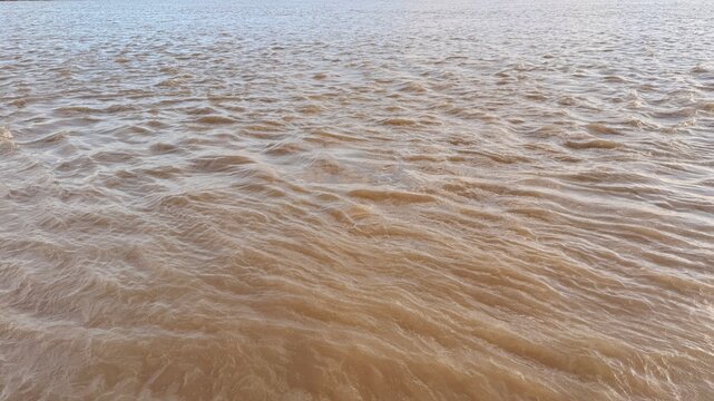 Brown murky river water flows with small choppy waves across the wide expanse
