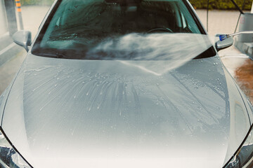 Washing a Silver Car at a SelfService Car Wash Station Under Bright Sunlight with Attention to...