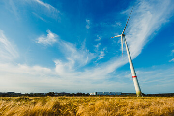 This scenic landscape showcases a towering wind turbine set against the backdrop of a clear blue...