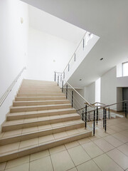 Staircase with metal railings in the lobby of a building with white walls. Vertical photo.