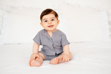 smiling baby on a white bed after sleeping, cute baby in a gray cotton bodysuit on a bed, space for...