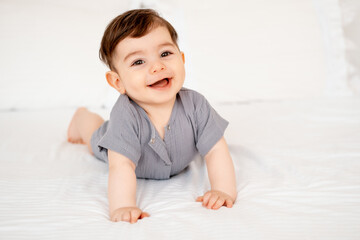 smiling baby on a white bed after sleeping, cute baby in a gray cotton bodysuit on a bed, space for...