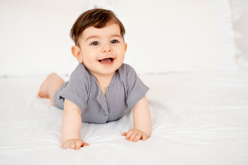 smiling baby on a white bed after sleeping, cute baby in a gray cotton bodysuit on a bed, space for...