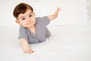 smiling baby on a white bed after sleeping, cute baby in a gray cotton bodysuit on a bed, space for...