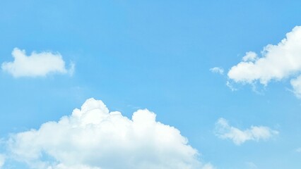Bright blue sky with fluffy white cumulus clouds, indicating a clear and bright day. Nature background, blue sky with white clouds.