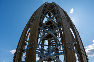 Top of Tokaj observation tower shaped like a wine barrel near Malá Tŕňa, Slovakia. Wooden and steel spiral structure with sun shining behind, under clear blue sky.