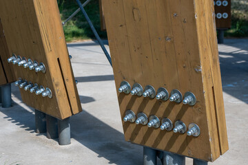 Close-up of metal bolts and washers securing wooden beams to steel supports on concrete base. Outdoor structure detail in bright daylight.