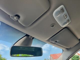 This image depicts the interior view of a car roof, showcasing the rearview mirror alongside the...