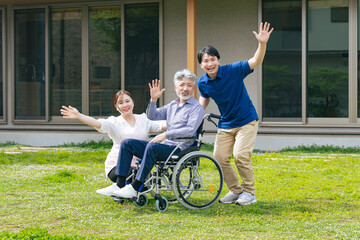 住宅の前で手を振る車椅子に乗ったシニア男性とケアスタッフ