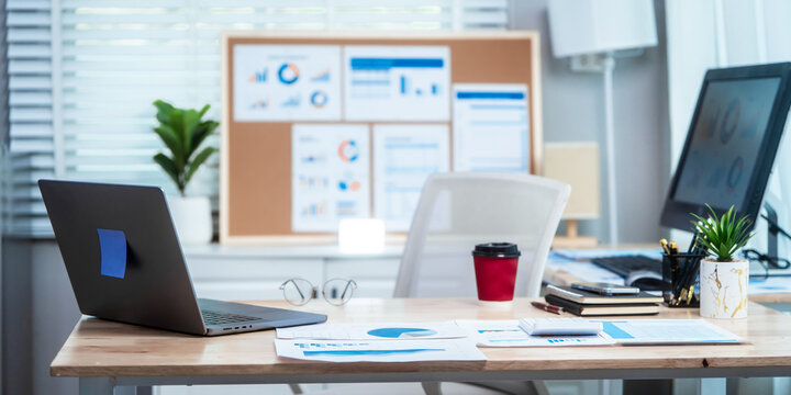 Neatly arranged office workspace features desk with computer, laptop, documents, charts, pinboard, representing professional, business environment ready for efficient work and information management