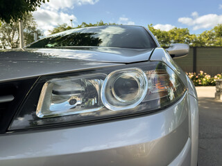 A shiny silver car headlight, meticulously designed, stands out against a bright blue sky, creating a visual contrast that captivates automotive enthusiasts and photographers with its beauty