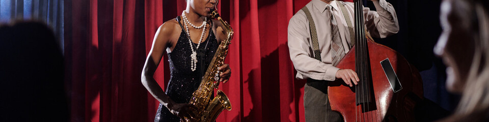 Black young adult woman playing saxophone and Caucasian middle aged man playing double bass...