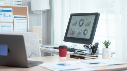 Neatly arranged office workspace features desk with computer, laptop, documents, charts, pinboard,...