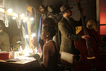 Black young adult woman sitting at dressing table preparing for performance, middle aged Caucasian...
