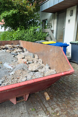 Construction Waste Disposal A rented skip bin overflowing with various building debris can be found...