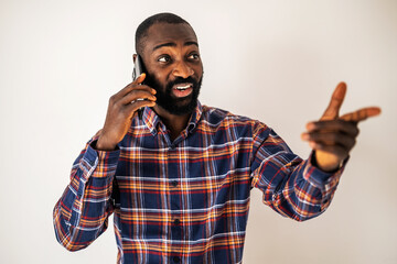 Cheerful black man in cozy shirt standing in front of wall and talking on mobile phone.