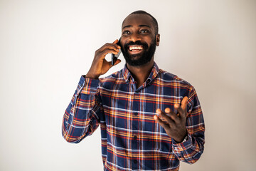 Cheerful black man in cozy shirt standing in front of wall and talking on mobile phone.