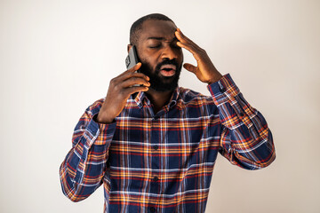 Anxious and tired black man in cozy shirt standing in front of wall and talking on mobile phone.
