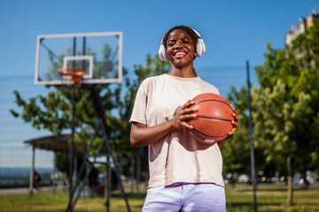 Young woman practicing basketball alone at sports court in the morning. Happy girl playing basketball and listening music on sunny day.