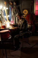 Middle aged Caucasian man wearing suit and hat sitting at dressing table reading sheet music in jazz club backstage area, with upright bass and stage costumes visible in background