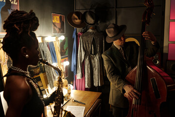 Black woman young adult playing saxophone with Caucasian middle aged man performing on double bass...