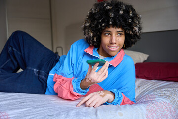 Young student using voice assistant on smartphone while relaxing on bed