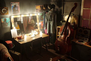 Musicians dressing room featuring upright bass, vintage reel-to-reel tape recorder, illuminated vanity mirror, jazz posters on wall, stage costumes hanging on rack © pressmaster