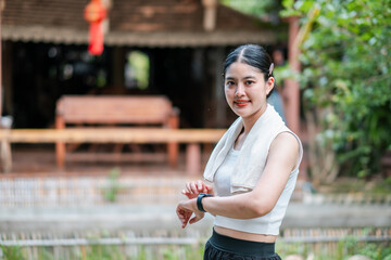 A young woman in sportswear with a fitness tracker, standing outdoors in a natural setting, smiling...
