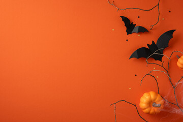 Halloween-themed image featuring black paper bats, orange pumpkins, and branches against an orange...