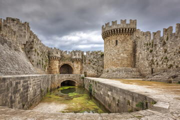 Medieval fortress of rhodes with stone walls, gate, and moat under cloudy sky