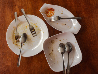A collection of empty plates along with spoons and forks placed on a wooden table, showing the...