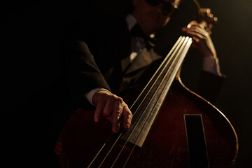 Middle aged Caucasian man wearing suit and sunglasses playing double bass on stage, close up of...