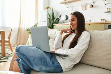 Charming young woman enjoys a quiet afternoon at home while working on her laptop