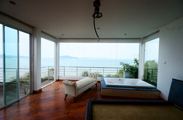 Empty abandoned coastal room with panoramic ocean view, white sofa, jacuzzi, and wooden floor in...