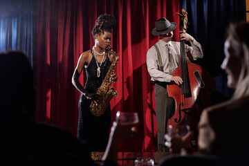 Black young adult woman playing saxophone and Caucasian middle aged man playing double bass...