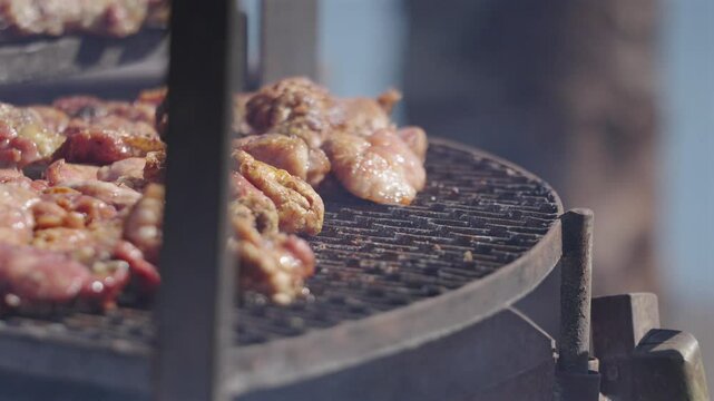 Man's hand with tongs arranging grilled meat asado and chinchulines. Traditional Argentine food with burning and smoking firewood, close up