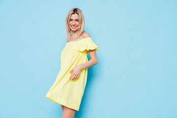 Young beautiful smiling blond female in trendy summer yellow dress clothes. Carefree woman posing...