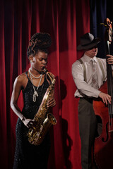 Black young adult woman playing saxophone next to Caucasian middle aged man performing on double...