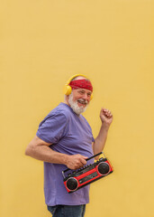 Happy senior man dancing and listening to music with a boombox and headphones on yellow background