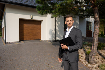 Real estate agent with clipboard standing in front of modern house