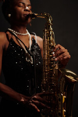 African American female musician playing saxophone on stage, wearing jewelry and performing jazz...