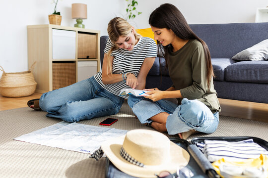 Two young happy female friends planning their next summer trip at home. Travel and vacation lifestyle concept.