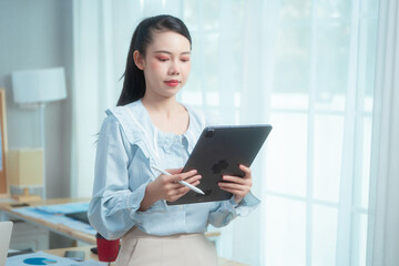 Obraz premium Confident beauty Asian office woman in a formal blouse hard working at her desk, reviewing a document with focus and a pen in hand. The workspace includes charts, a laptop, and a desktop computer.
