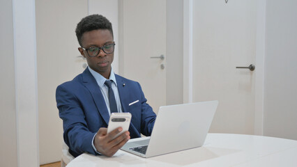 African Businessman Checking Phone at Desk