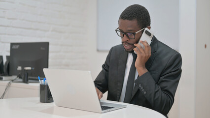 Professional African American businessman on an urgent phone call, focused at his laptop