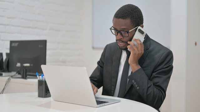 Professional African American businessman on an urgent phone call, focused at his laptop